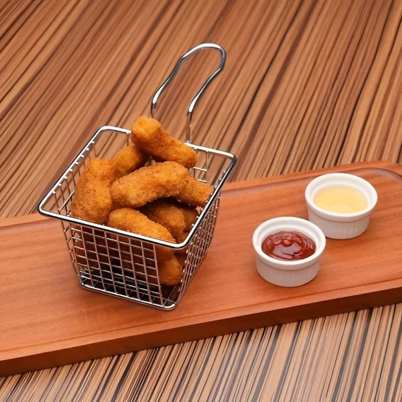 Crispy fried chicken nuggets in a metal basket with ketchup and mayonnaise on a wooden board.