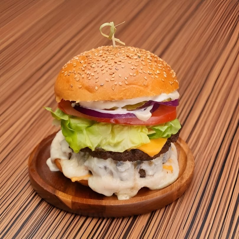 A Platan Restaurant burger with melted cheese, lettuce, tomato, onion, and pickles on a wooden plate.